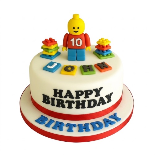 White fondant cake with a yellow and red block-style figure, colourful stacked blocks, and "Happy Birthday" text.