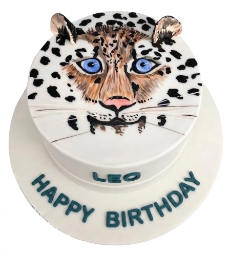 Round white cake with a detailed leopard face, blue eyes, black spots, and 3D ears, with a custom message.