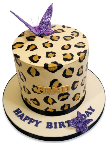 Round leopard print birthday cake with black and gold spots, purple glitter butterflies, and a custom name.