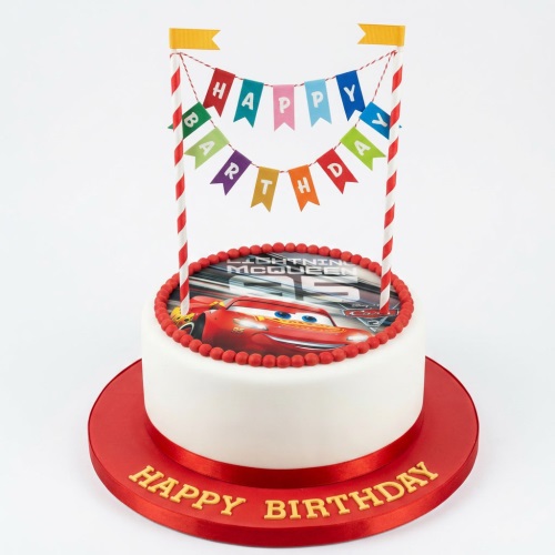Round white cake with Lightning McQueen edible image, red beads, and a 'Happy Birthday' banner topper.