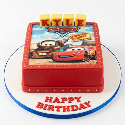 Red Disney Cars themed birthday cake with Lightning McQueen and Mater edible image, yellow name blocks, and silver pearl details.