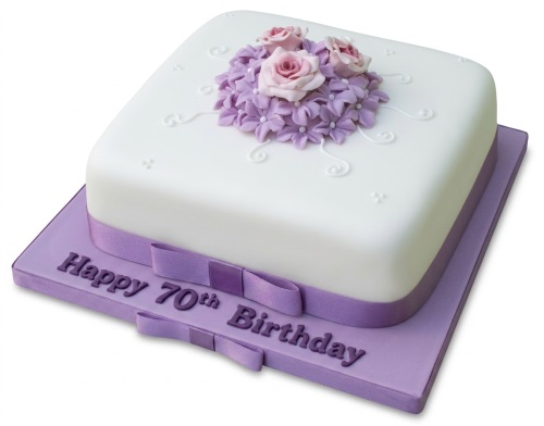 White square 70th birthday cake with purple ribbon and pink and purple sugar flowers.