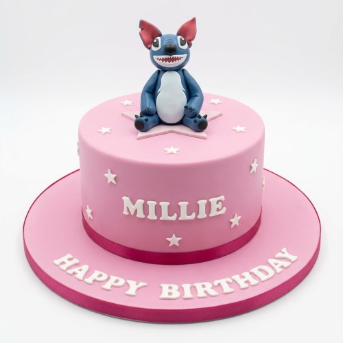 Pink round birthday cake with Stitch character topper and white stars, personalised with a name.
