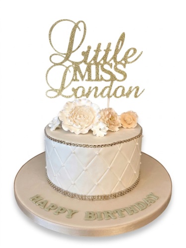 White quilted birthday cake with peach and white sugar flowers and a gold glitter topper.