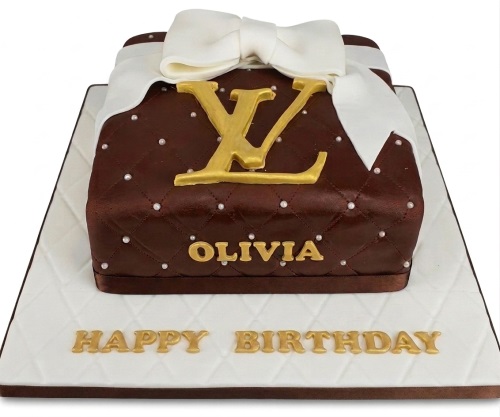 Brown luxury handbag cake with gold logo, white pearls, and a white bow.