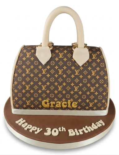 Brown designer handbag shaped cake with gold monogram, cream handles, and custom message.