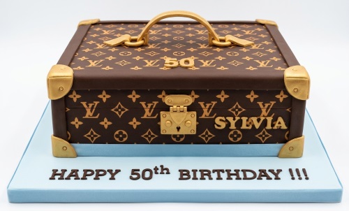 Brown and gold luxury suitcase birthday cake with designer monogram, golden hardware, custom age topper, and personalised name.