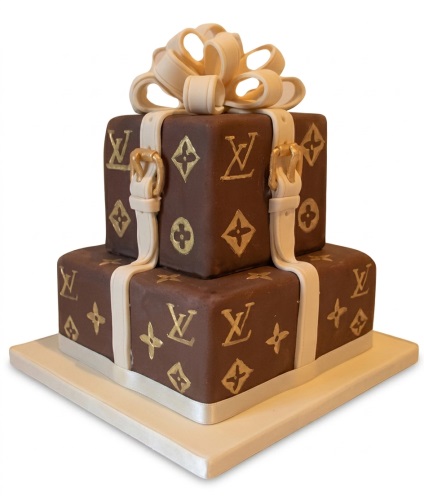 Two-tier brown and gold designer cake with LV style monogram, straps, and a cream bow.