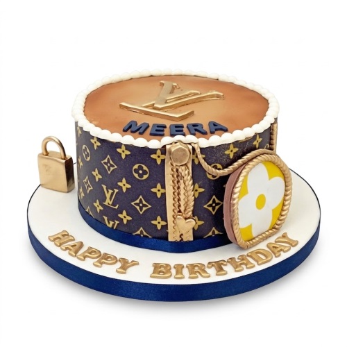 Round LV branded birthday cake with gold logo, padlock, and chain details, on a white board with a blue ribbon.