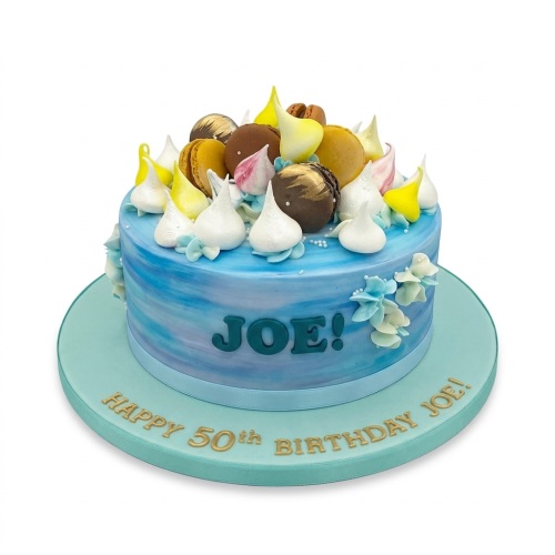 Round blue watercolour birthday cake with macarons, meringue kisses, and custom message.