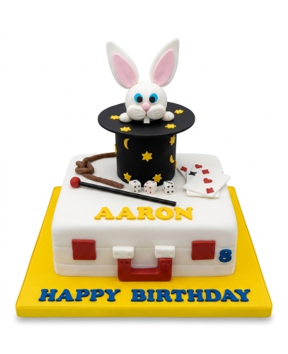 Two-tier magic show themed birthday cake with a rabbit in a top hat, playing cards, dice, and a magic wand.