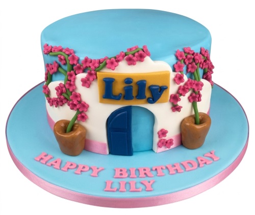 Round birthday cake with blue and white house design, pink floral decorations, a yellow name plaque, and a custom message.
