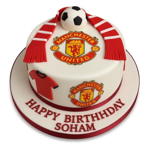 White round cake with Manchester United crests, red and white scarf, football, and red shirt decoration.
