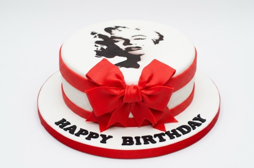 White round birthday cake with a black Marilyn Monroe silhouette, red ribbon, and a large red bow.