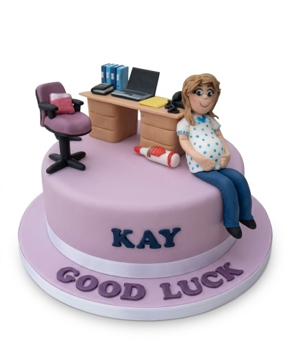 Round lilac cake with a pregnant woman figure, office desk, chair, and 'Good Luck' message.