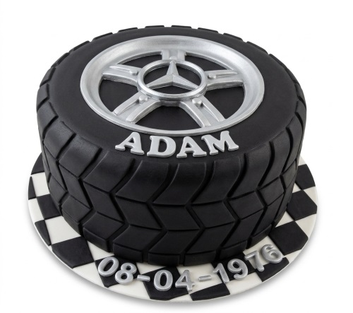 Black car tyre birthday cake with silver wheel rim, personalised name, and custom date on a chequered board.