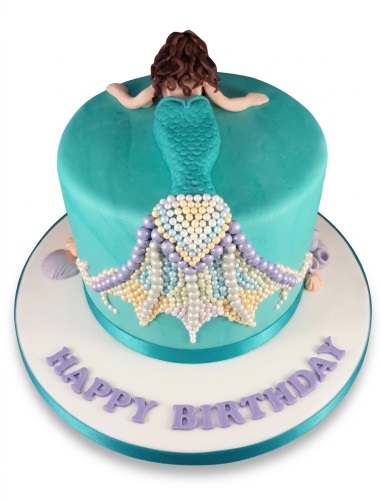 Round teal mermaid birthday cake with a brown-haired mermaid figure and a beaded tail, with "Happy Birthday" written on the cake board.
