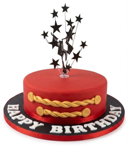Red round birthday cake with gold braids, gold buttons, and a black starburst topper on a black base with 'Happy Birthday' in white letters.