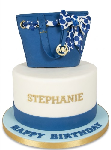 Two-tier birthday cake with a blue Michael Kors style handbag on top and a personalised name.