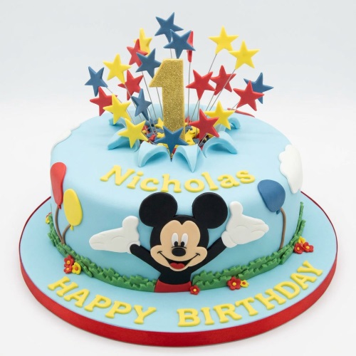 Round light blue Mickey Mouse 1st birthday cake with star toppers, balloons, and custom name.