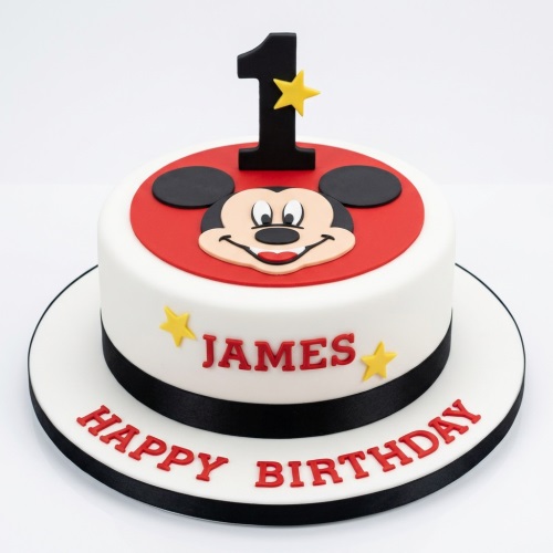 Round white fondant cake with a red top featuring Mickey Mouse face, a black number 1 topper with a yellow star, yellow stars, and a black ribbon.