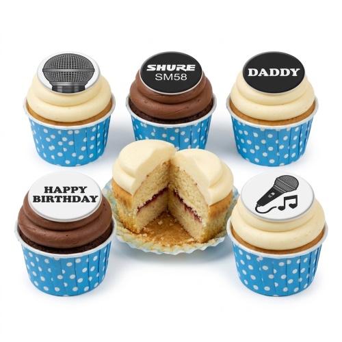 A set of cupcakes with white and chocolate frosting in blue polka dot wrappers, topped with edible microphone designs, a 'Shure SM58' logo, 'DADDY', and 'Happy Birthday' messages. One cupcake is cut to show vanilla sponge and jam filling.