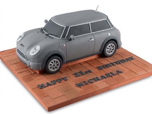 Grey Mini Cooper car birthday cake on a brown brick-patterned cake board with custom message.