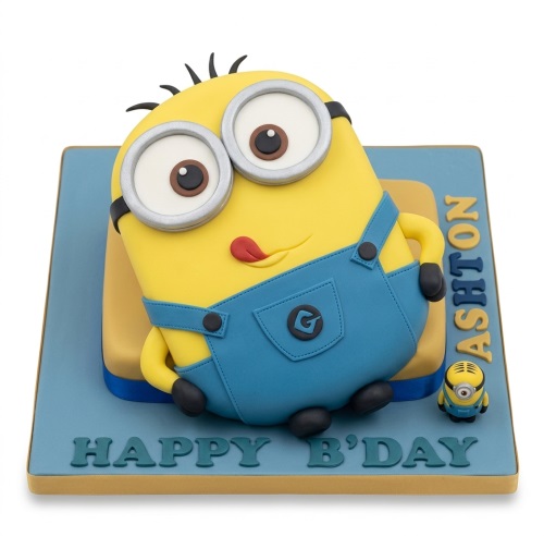3D Minion character birthday cake with yellow body, blue overalls, goggles, and a small Minion figurine.