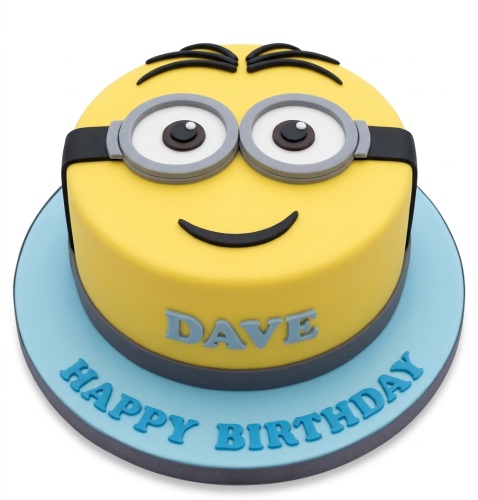 Round yellow Minion face birthday cake with goggles and a smile, on a blue board.
