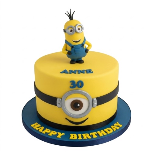 Round yellow Minion themed birthday cake with a Minion character topper, goggle design, and space for custom name and age.