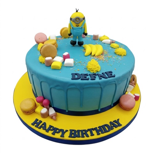 Round blue Minion birthday cake with a Minion figurine, bananas, macarons, and colourful sweets.