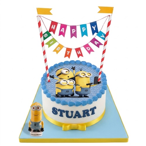 Round white Minions birthday cake with blue icing, Minion figures, Happy Birthday banner, and a personalised name.