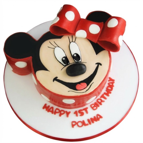 Round Minnie Mouse head birthday cake with red polka dot bow and base, on a white cake board.