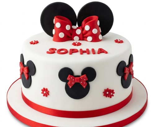 Round white Minnie Mouse themed birthday cake with black ears, red polka dot bow, and red decorations.