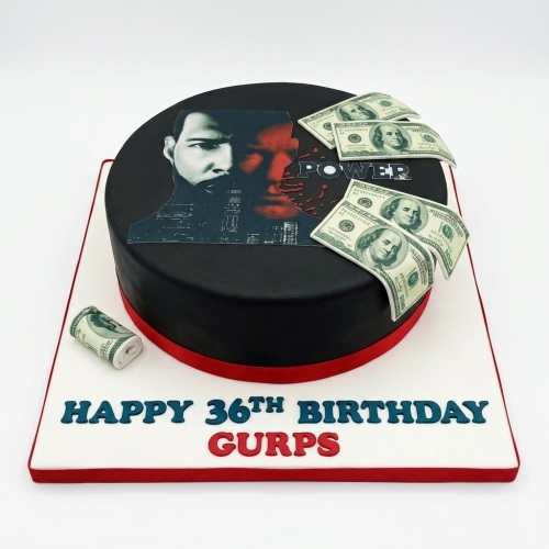 Round black birthday cake with Power TV show character image and edible dollar bills, red ribbon base.
