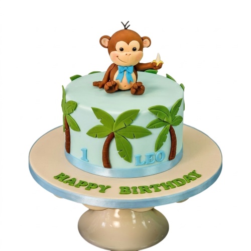 Light blue round birthday cake with a monkey figurine, palm trees, and a custom age and name.
