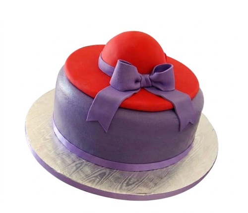 Round purple cake with a red hat and purple bow decoration on top.