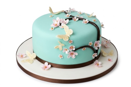 Round light blue cake decorated with pink sugar cherry blossoms, gold pearl centres, and cream butterflies.