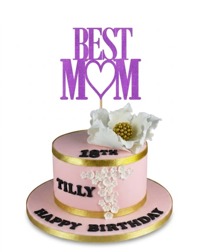 Pink round birthday cake with white sugar flowers, gold ribbon, and a "BEST MOM" topper.