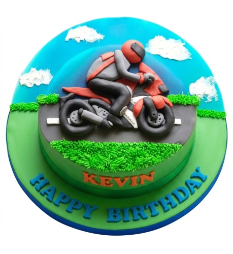 Round two-tier cake with a 3D fondant motorcyclist on a motorcycle, road, green grass, and blue sky with clouds.