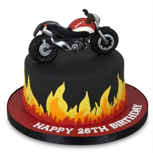 Black birthday cake with a red and black Ducati motorcycle topper and orange and yellow flames around the base.