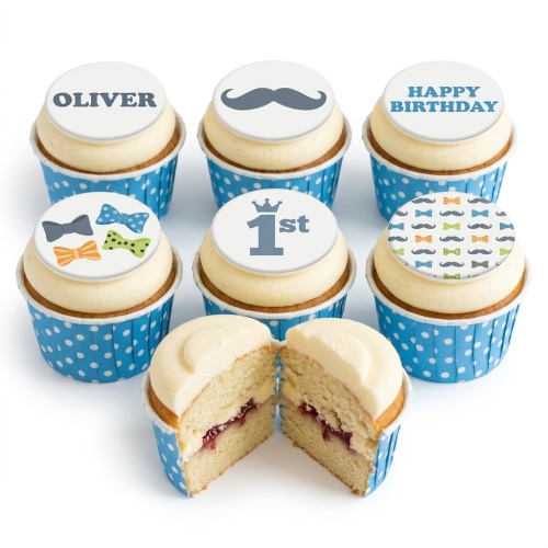 Six cupcakes with white icing, blue polka dot wrappers, and edible toppers featuring mustaches, bow ties, and a custom age.