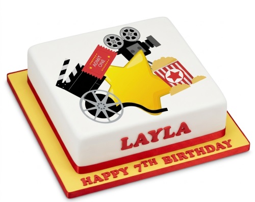 White square birthday cake with movie theme decorations including a film camera, clapperboard, film reel, popcorn, and a yellow star.