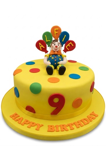Yellow birthday cake with clown topper, colourful polka dots, balloons, and custom age number.