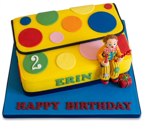 Yellow rectangular birthday cake with colourful polka dots, a clown figurine, and a custom age topper.
