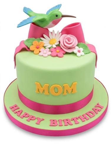 Light green round cake with pink ribbon, sugar flowers, and a green hummingbird topper.
