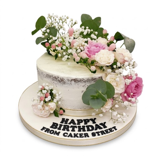 Round semi-naked birthday cake decorated with pink and white roses, baby's breath, and eucalyptus leaves.