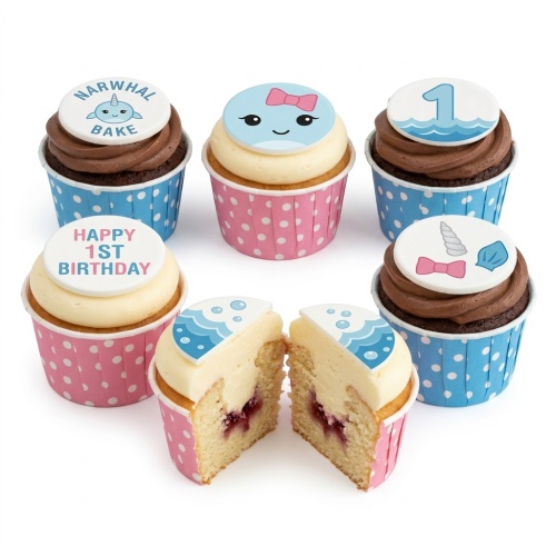 Assortment of narwhal themed 1st birthday cupcakes with pink and blue polka dot wrappers, featuring 'Happy 1st Birthday' and number '1' toppers.