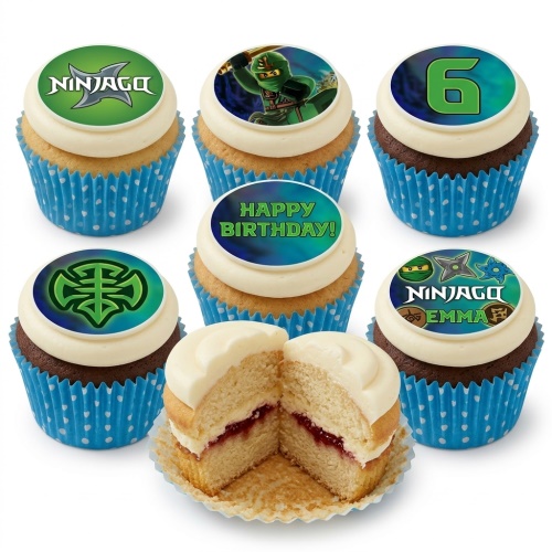 A selection of Ninjago themed cupcakes with green and blue edible toppers, featuring Ninjago logos, characters, and custom age/message examples, in blue polka dot cases. One cupcake is cut to show a vanilla sponge with jam.