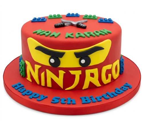 Red Ninjago themed birthday cake with yellow ninja mask, Lego bricks, and ninja swords.